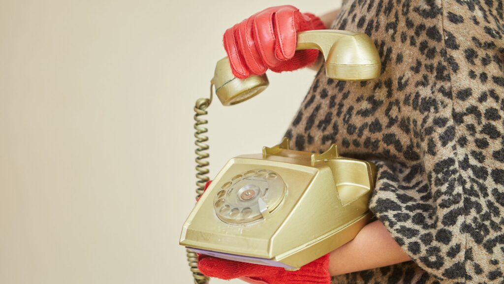 Woman with red gloves holding rotary phone.