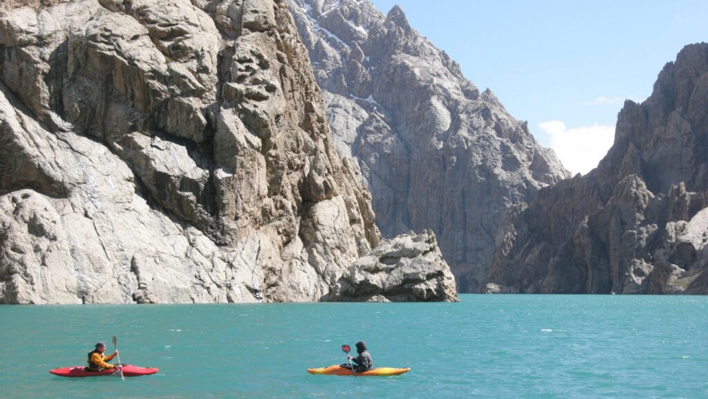 Kayakers on an alpine lake surrounded by rocky mountains.