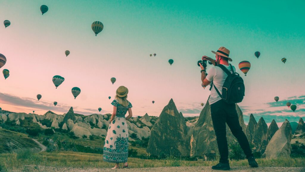 Woman being photographed in front of hundreds of hot air balloons.